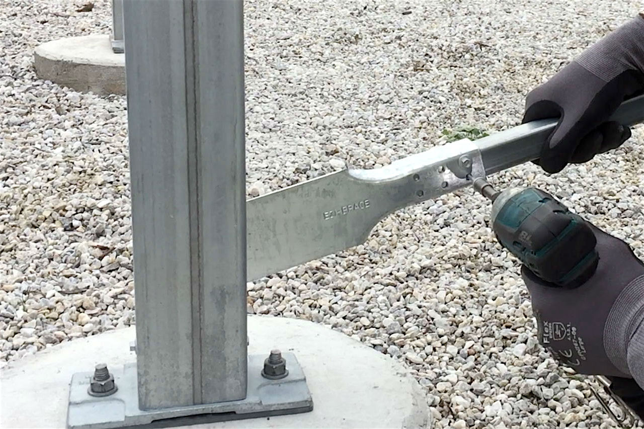 Ezibrace paddle attached to a steel SHS post with a person holding a drill attaching the other end of the paddle to the 30mm SHS post to form the crossbrace.